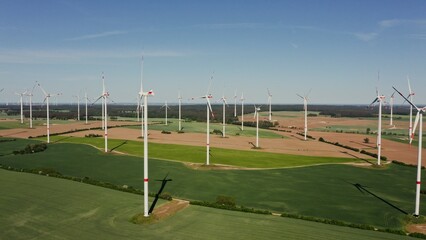 Fototapeta premium Many working wind turbines among the green fields. Video from a drone on a summer sunny day.