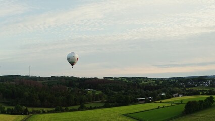 Obraz premium Drone shot of a hot air balloon in the sky flying over a green valley near a village in Germany on a sunny day.