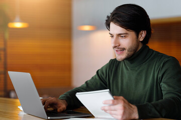 Famous male blogger working on new article, using laptop at cafe, empty space