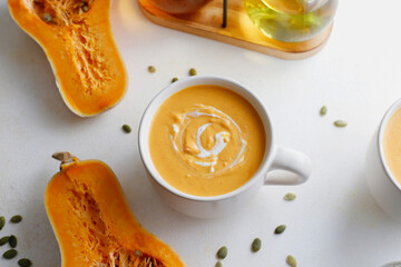 Roasted butternut squash soup with cream and pumpkin seeds on two white mugs.