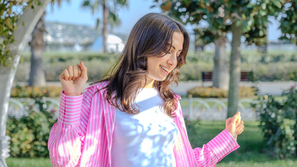 Obraz premium A young brunette businesswoman in a tree-filled park on a spring day, looking at the camera while dancing
