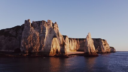 Picturesque sheer cliffs of limestone and flint with photogenic natural arches, washed by the waters of the English Channel in the red rays of the setting sun. Etretat, France