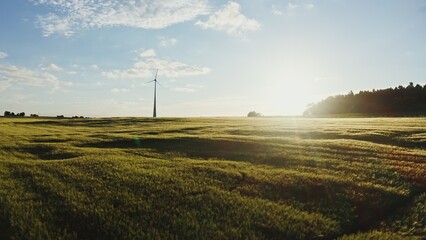 The drone quickly flies towards the wind turbine, standing on a picturesque green meadow,...