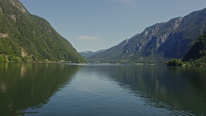 A picturesque lake located in a lowland between gently sloping mountains overgrown with a dense spruce forest. Panoramic video from a drone on a summer sunny day. Austria