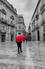 Man walking through Italian plaza with red umbrella 