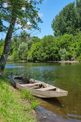Small wooden unpainted boat in the Dordogne river near the village of Carennac in Lot Occitanie Southern France under a blue sky in summer. 