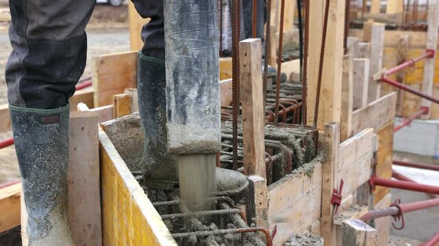 Construction workers with concrete boom pump crane at new house construction site pouring concrete into a formwork with reinforcement for building walls