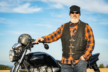 Obraz premium Cooler Motorradfahrer mit passendem Outfit steht stolz bei seiner Maschine.