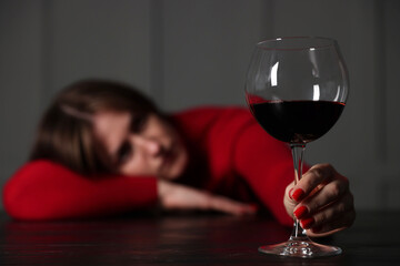 Alcohol addiction. Woman with glass of red wine at wooden table indoors, selective focus