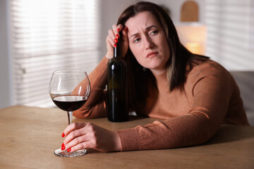 Alcohol addiction. Miserable woman with wine at table indoors, selective focus
