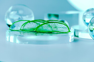Aloe slices rest on a glass base surrounded by clear spheres, creating a calming spa atmosphere.