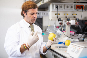 Geneticist working in laboratory, injecting additives into apple during experiments with...