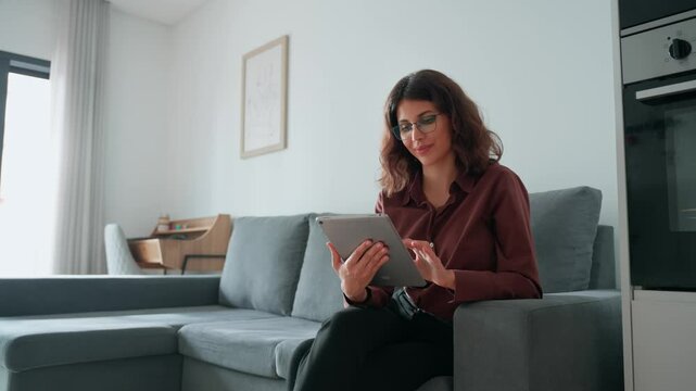 Latin hispanic girl holding tab gadget, working on digital online AI IT project at home. Freelance business woman sitting on couch sofa using tablet computer application for work remotely. Copy space