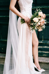 Bouquet of flowers in the hand of a bride standing on the threshold of an old house. Cropped....