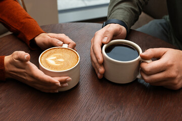 Colleagues having coffee break at wooden table in cafe, closeup