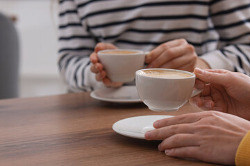 Coffee break. Women with cups of hot drinks at wooden table indoors, closeup