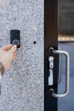 Close-up of a person's hand holding a keychain with a key fob near a key reader access device on a granite building&rsquo;s exterior wall next to glass door, showcasing security and smart access technology