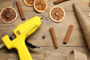 Hot glue gun and handicraft materials on wooden background, flat lay