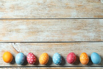 Beautiful decorated Easter eggs on light wooden table, flat lay. Space for text