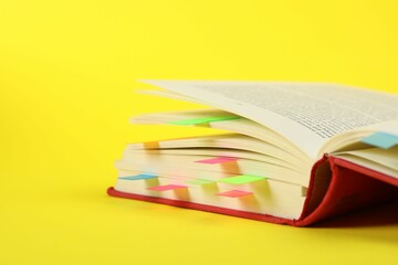 Book with colorful tabs on yellow background, closeup. Space for text