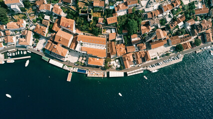 Promenade with a swimming pool and a private beach near old houses with red roofs. Perast, Montenegro. Drone