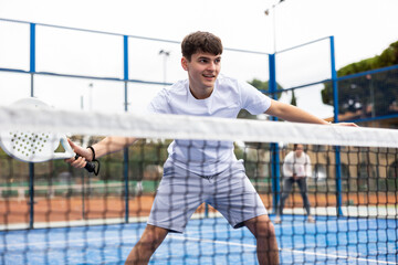 Young European male player serving ball during training padel in court outdoors in spring