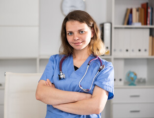 Skillful woman physician standing in her office and looking at camera.