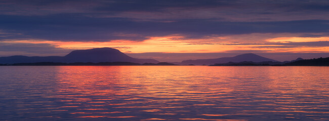 Nature in Norway. Panoramic view of the fjord. Bright sunshine during sunset. Vacation and travel in summer north. Mountains and reflections on the surface of the water.