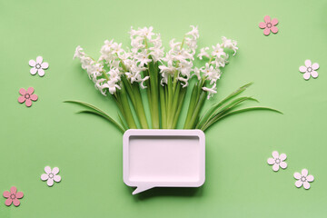 White hyacinth flowers arranged in a speech bubble-shaped vase on a green background with decorative pink and white flowers, symbolizing spring and communication