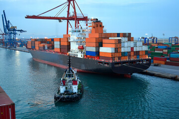 Fototapeta premium Cargo Ship and Tugboat at Twilight in a Busy Port with Cranes