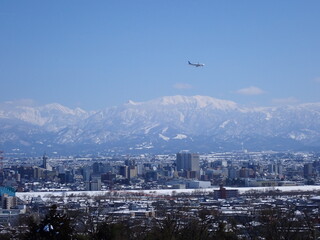 2025年2月25日雪景色の富山市街地と冠雪の北アルプ氏と旅客機