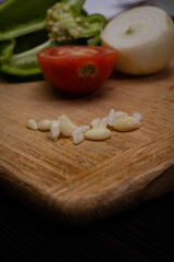 Tomatoes, peppers and onions on a cutting board on a dark background, Preparation of a vegetable salad with fresh tomatoes, pepper, garlic and onions. Chopped garlic on a wooden cutting board and fres