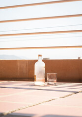 Glass of water and bottle on the balcony with blinds in the background, Glass and bottle of vodka on the balcony, shallow depth of field