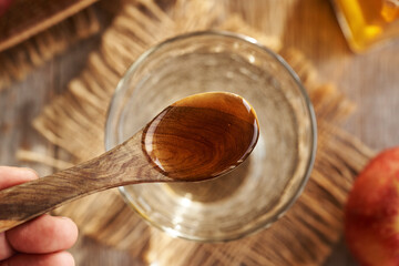 Apple cider vinegar on a wooden spoon above a glass of water