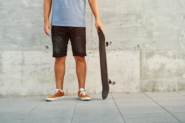 Unrecognizable skater holding skateboard by concrete wall
