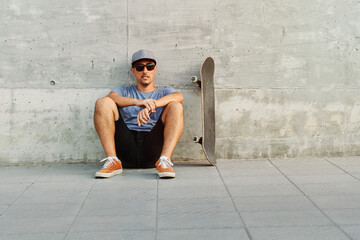 Skateboarder relaxing against concrete wall after skating session