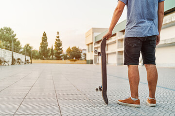 Unrecognizable skater holding skateboard in urban environment at sunset