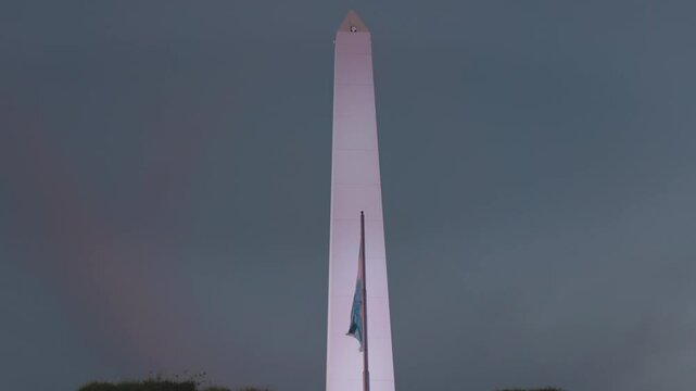 a close up shot of the historic obelisk of buenos aires and the argentinian flag at dusk