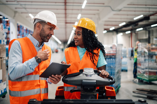 Warehouse workers discussing logistics using tablet on forklift