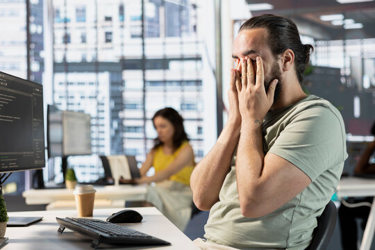 Exhausted man at work rubbing eyes, creating machine learning models that can process and analyze data. Tired IT expert programming in office, struggling to stay awake after pulling all nighter
