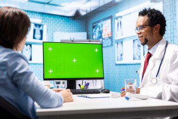 General practitioner consulting a female patient next to isolated chroma key display on pc, sharing...