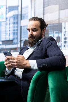 Ambitious powerful entrepreneur reviewing financial market trends, surfing the internet on his mobile phone and ensuring company productivity. Global enterprise success story.
