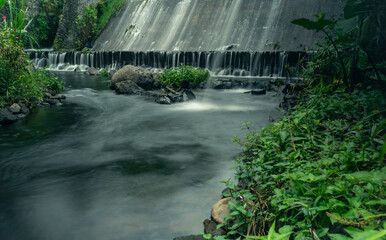 Beautiful small river long exposure shot with rock and manmade dam waterfall