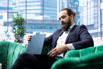 Focused determined administrator works on his laptop in the office, reviewing investment...