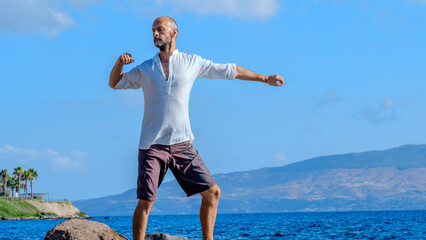 A middle-aged charismatic man, wearing a white shirt, is relaxing and enjoying the sun by doing...