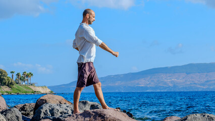 A middle-aged charismatic man, wearing a white shirt, is relaxing and enjoying the sun by doing...