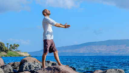 A middle-aged charismatic man, wearing a white shirt, is relaxing and enjoying the sun by doing...