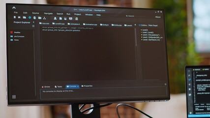 Asian programmer seen typing code for a user interface design on dual monitors, working in a...
