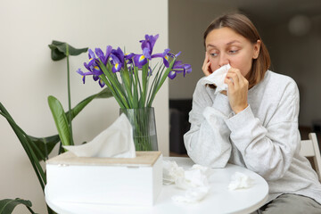 Sick unhealthy allergic young woman covering nose with paper tissue has runny stuffy nose, sneezes...