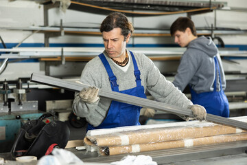In glass workshop, man glazer works with glass sheets and related supporting parts, preparing PVC...